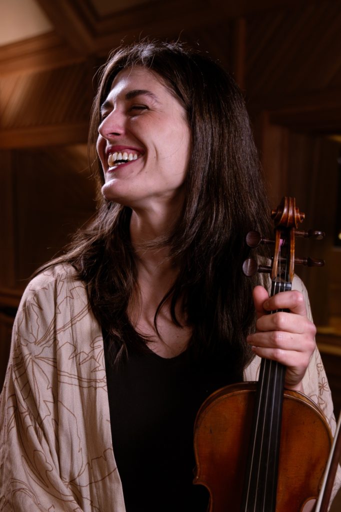 Mathilde Fillat sorridente: branca de cabelo castanho liso. Veste blusa preta, casaco creme e segura um violino.