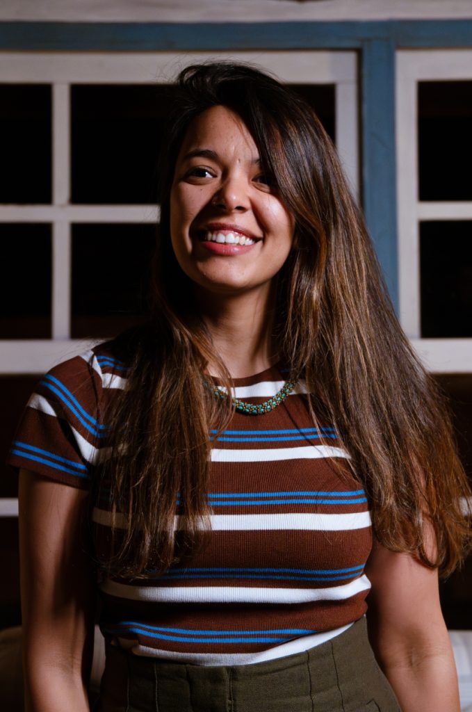 Mônica Morais: parda de cabelo longo liso castanho. Veste camiseta listrada.